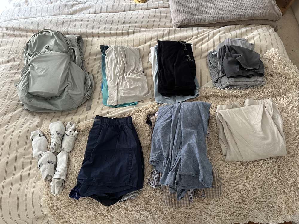 Clothes folded and laid out on the bed beside a rucksack, half way through packing